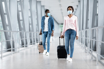 Fototapeta na wymiar Pandemic Travels. Black People In Masks Walking With Luggage At Airport Terminal