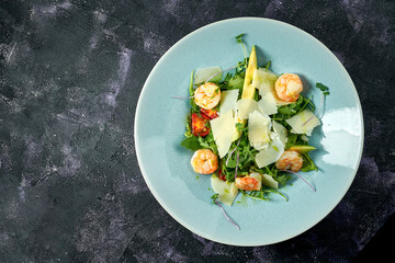 Salad with arugula, shrimps, parmesan and avocado in a blue plate on a black background