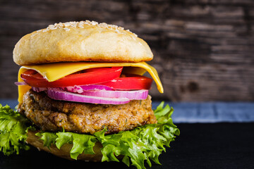 Fresh delicious homemade veggie burger lies on natural slate on rustic wooden background. Delicious tasty burger with lettuce, cheese, onion and tomato. buckwheat and lentil cutlet