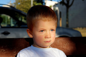 Portrait of a charming blond boy. A three-year-old boy with tears in his eyes. Sad boy looks into...