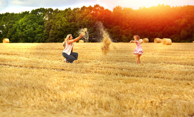 Banner with mom and daughter caucasians together on a mown wheat field throw hay where there are huge sheaves. Family fun and fun. Nature. Harvesting. Agriculture. Travel and vacation concept