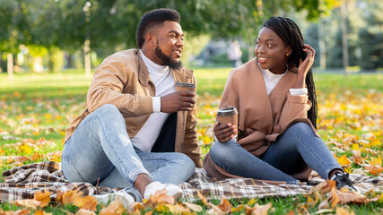 Happy couple drinking coffee while resting on plaid in autumn park