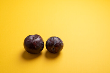 Pair of purple plums on mustard yellow desk. Couple of blue plums with bright yellow background. Ready for adding text