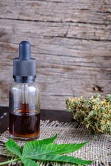 brown medical cannabis resin extract in bottle of medicine dropper. next to marijuana buds and hemp leaf. on hemp sack. Wooden backdround on rust metal suface. vertical