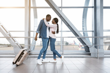 Fototapeta na wymiar Ready For Honeymoon Travel. Romantic African Couple Hugging At Airport Terminal