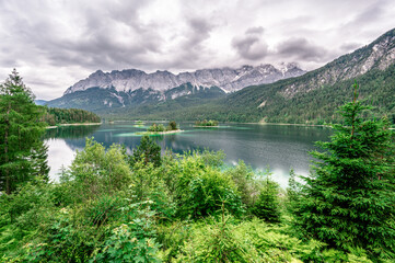 Small islands with pine-trees in the middle of Eibsee lake with Zugspitze mountain. Beautiful landscape scenery with paradise beach and clear blue water in German Alps, Bavaria, Germany, Europe.