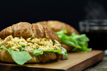 Close up Croissant stuffed scrambled eggs on wooden tray with hot coffee background.
