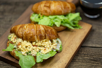 Croissant stuffed scrambled eggs on wooden tray with hot coffee background.