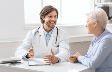 Fototapeta premium Friendly geriatrician talking with female patient, filling medical history