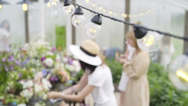 women group arranges festive bouquets at large table taking part at interesting floral masterclass in greenhouse focus on glowing lamp garland