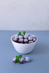 Frozen cherries with sprigs of mint in a white bowl on a gray background. Copy space. Vertical orientation.