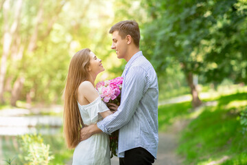 Fototapeta premium Lovely girl with bouquet of peonies hugging her boyfriend on romantic date at park