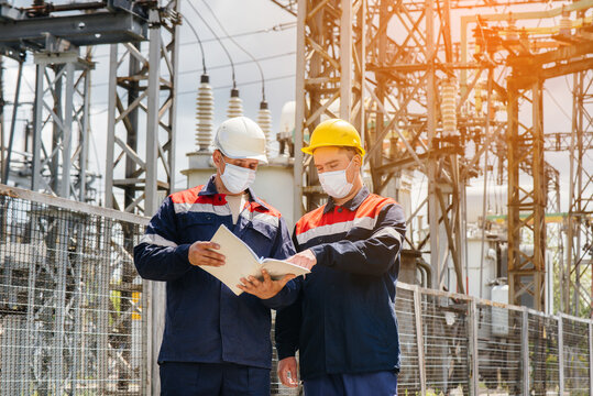 Engineers electrical substations conduct a survey of modern high-voltage equipment in the mask at the time of pandemia in the evening. Energy. Industry
