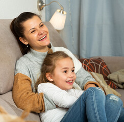 Happy woman laughing and tickle her daughter in home interior