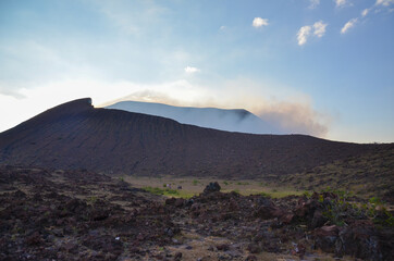 Fototapeta na wymiar Landscape of Telica active volcano in Nicaragua after a hike. View of the crater with steam during sunset. Red volcano surround of volcanic rocks. Adventure concept. 