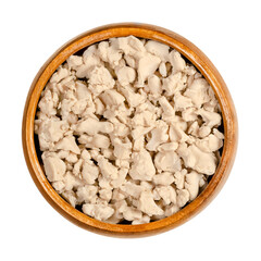 Crumbled fresh bakers yeast in a wooden bowl. Compressed fresh yeast, crushed with fingers, used in baking as a leavening agent. Saccharomyces cerevisiae. Close-up, from above, over white, food photo.