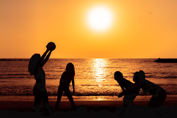 Happy girls playing to volleyball in the sea shore at sunset. Young people having fun on summer vacation. Travel, party and friendship concept. Image