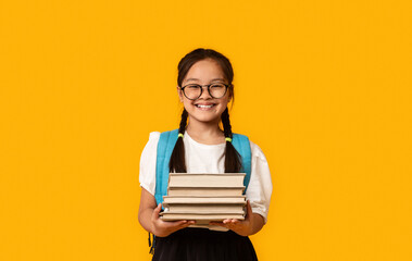 Cheerful Chinese Schoolgirl Holding Books Posing On Yellow Background