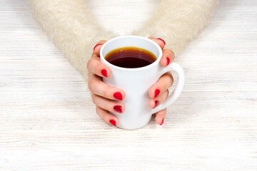 Female hands hold a white cup against the background of a white fluffy sweater with a beautiful red winter manicure. Drink, fashion, morning. New Year. Celebration. Tea coffee.