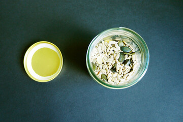 pumpkin, sunflower, sesame, Chia and flax seeds in a transparent glass jar with a metal lid next to the top view on a dark background