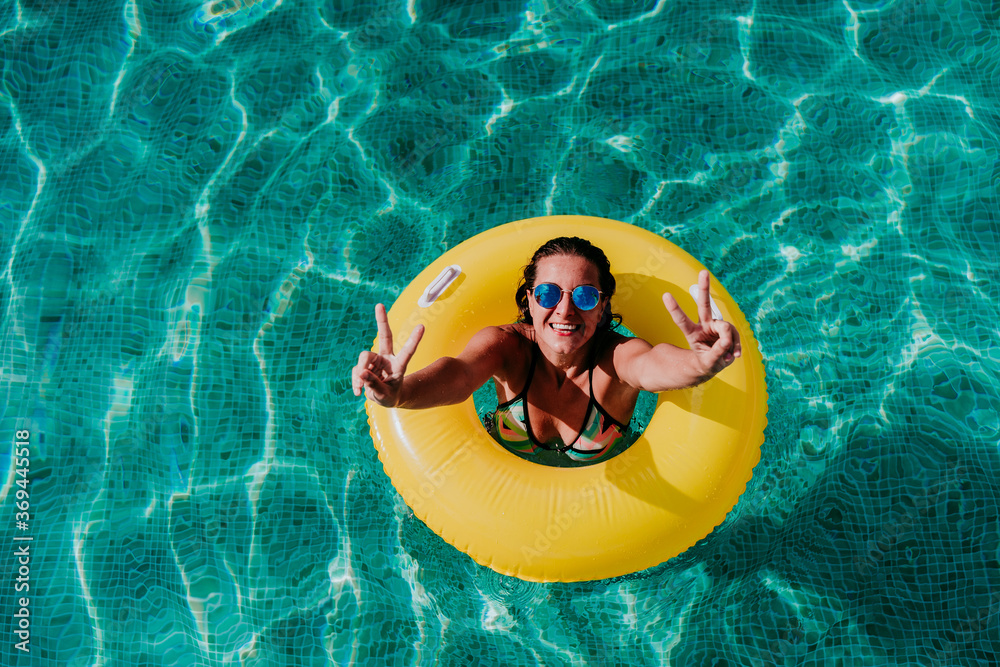 Wall mural top view of happy young woman floating in a pool in a yellow donuts. summer and fun lifestyle