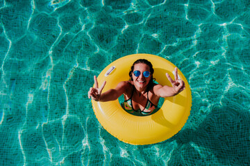 top view of happy young woman floating in a pool in a yellow donuts. summer and fun lifestyle