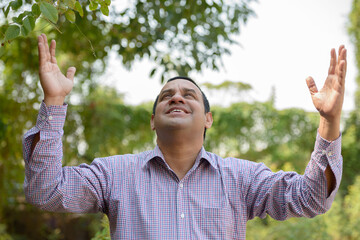 Portrait of happy overweight Indian businessman at the park outdoors