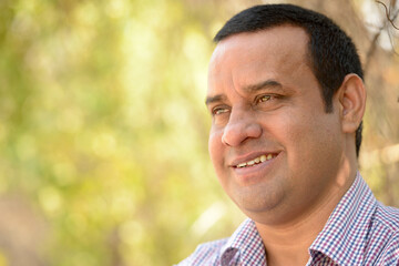 Portrait of happy overweight Indian businessman at the park outdoors