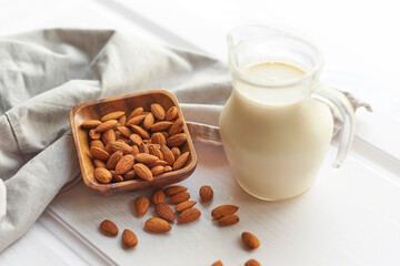 Almond milk in glass with almonds in wooden bowl on a white wooden table