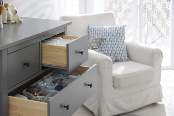 Modern open chest of drawers with clothes and accessories in baby room