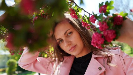 Fototapeta premium Portrait of pretty girl among branches of blossoming tree in spring in park