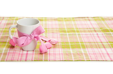 white cup with a pink ribbon on the tablecloth