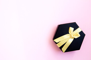 One dark black gift box with luxury gold bow on pink background. Horizontal with copy space. Flat lay