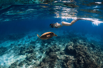 Woman with fins swimming underwater with big turtle.