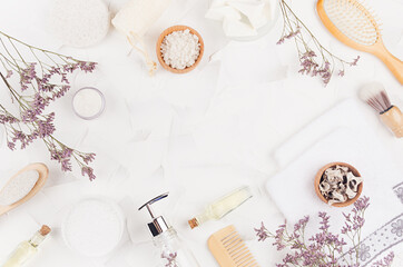Soft cosmetic products and natural accessories for skin cleansing and body care with dry small flowers on light white background, flat lay, frame.