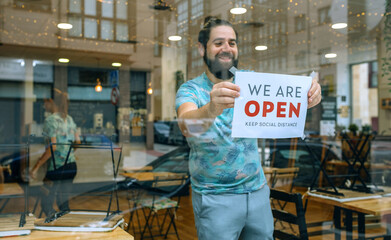 Happy man placing opening poster after coronavirus on the glass of his business