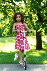 Little black girl with a kick scooter in a city park