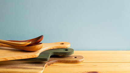 Wooden tray, cutting board, plate and spoons on wooden table with blue background