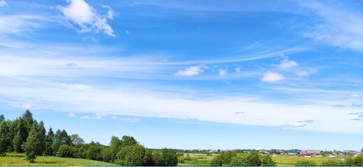Obraz na płótnie Canvas village landscape, green field and blue sky with small white clouds.