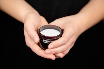 Female hands holding jar of shea butter cream over black. Skin and hair care natural cosmetics.