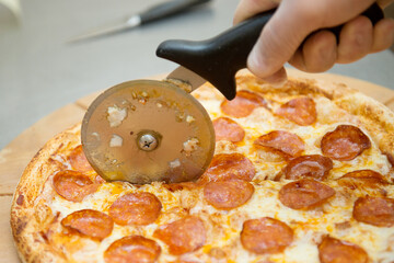 Pipperoni pizza is cut into pieces with a special knife, close-up.