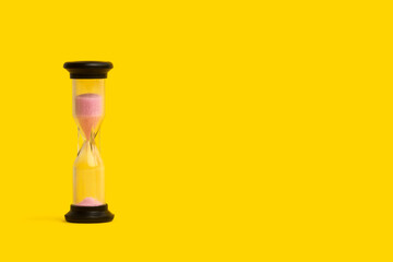 Reloj de arena sobre un fondo amarillo liso y aislado y brillante. Vista de frente. Copy space