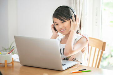 smiling asian girl student studying online using laptop and listen music sitting at home