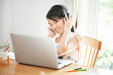 asian girl student studying online using laptop and listen music sitting at home