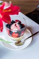 Dessert with cream and ice cream and fruits: strawberries, blueberries. In a cafe on a background of flowers