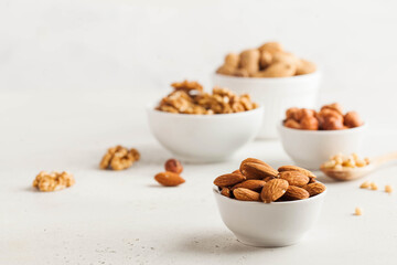 A handful of almonds in a white bowl, assorted nuts on a light background. Healthy snacks, healthy fats. Copy space.