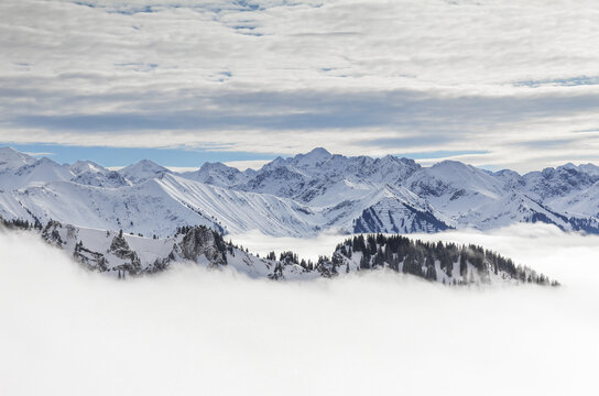 Snow covered mountains with inversion valley fog and trees shrouded in mist. Scenic snowy winter landscape in Alps, Allgau, Kleinwalsertal, Bavaria, Germany.