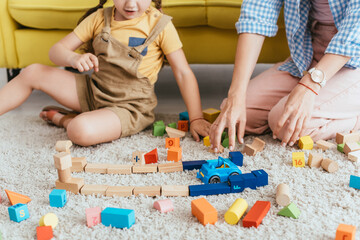 partial view of child and nurse playing with multicolored blocks and toy car on floor