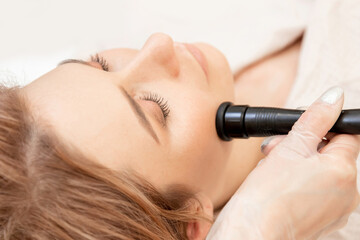 Fototapeta premium Young woman receiving RF lifting electric facial massage for face skin