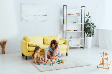 selective focus of babysitter and child playing with multicolored blocks on floor in living room